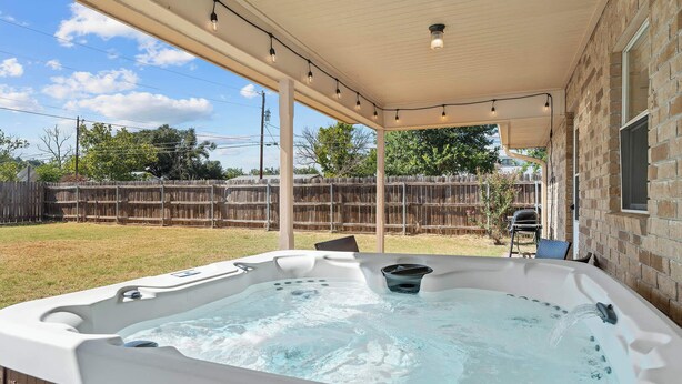 A hot tub under a covered patio with a wooden fence in the background.