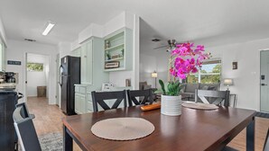 A modern kitchen with a dining area, a refrigerator, and a potted orchid.