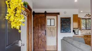 Een modern ingericht houten vakantiehuisje met een houten deur, een grijze bank en een schoolbord met een welkomstboodschap.