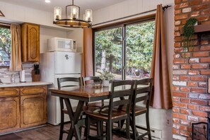 A kitchen with wooden cabinets, a white refrigerator, a dining table with chairs, and a large window with curtains. - Mountain Vista (Greer)