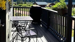 Een houten terras met een tafel en stoelen, met uitzicht op een meer en beboste heuvels.