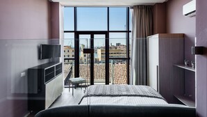 Quarto de hotel moderno com uma janela grande, uma cama, uma TV e um guarda-roupa.