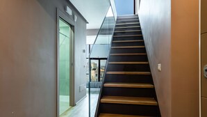Uma escadaria moderna com degraus de madeira e guarda-corpos de vidro, que dá acesso a um espaço interior luminoso.