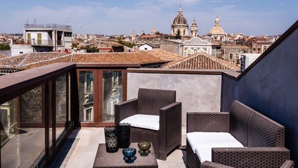 Terraço no telhado com móveis de vime, guarda-corpo de vidro e vista para a cidade.
