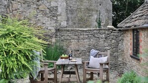 Un muro de piedra rústico, una mesa de madera y sillas en un jardín.