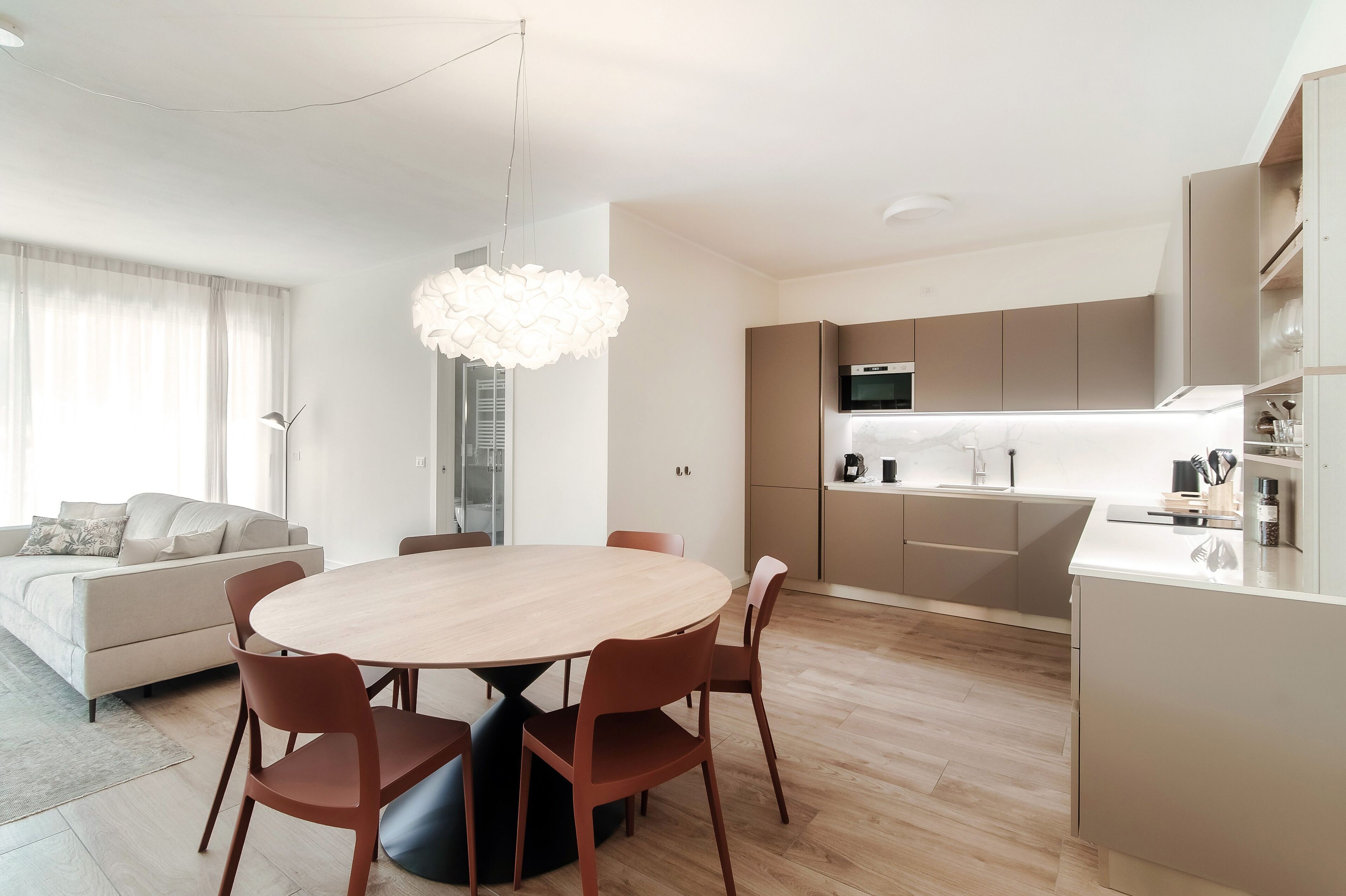 A modern kitchen with a built-in oven, a dining area with a round table and chairs, and a sofa in the living area.