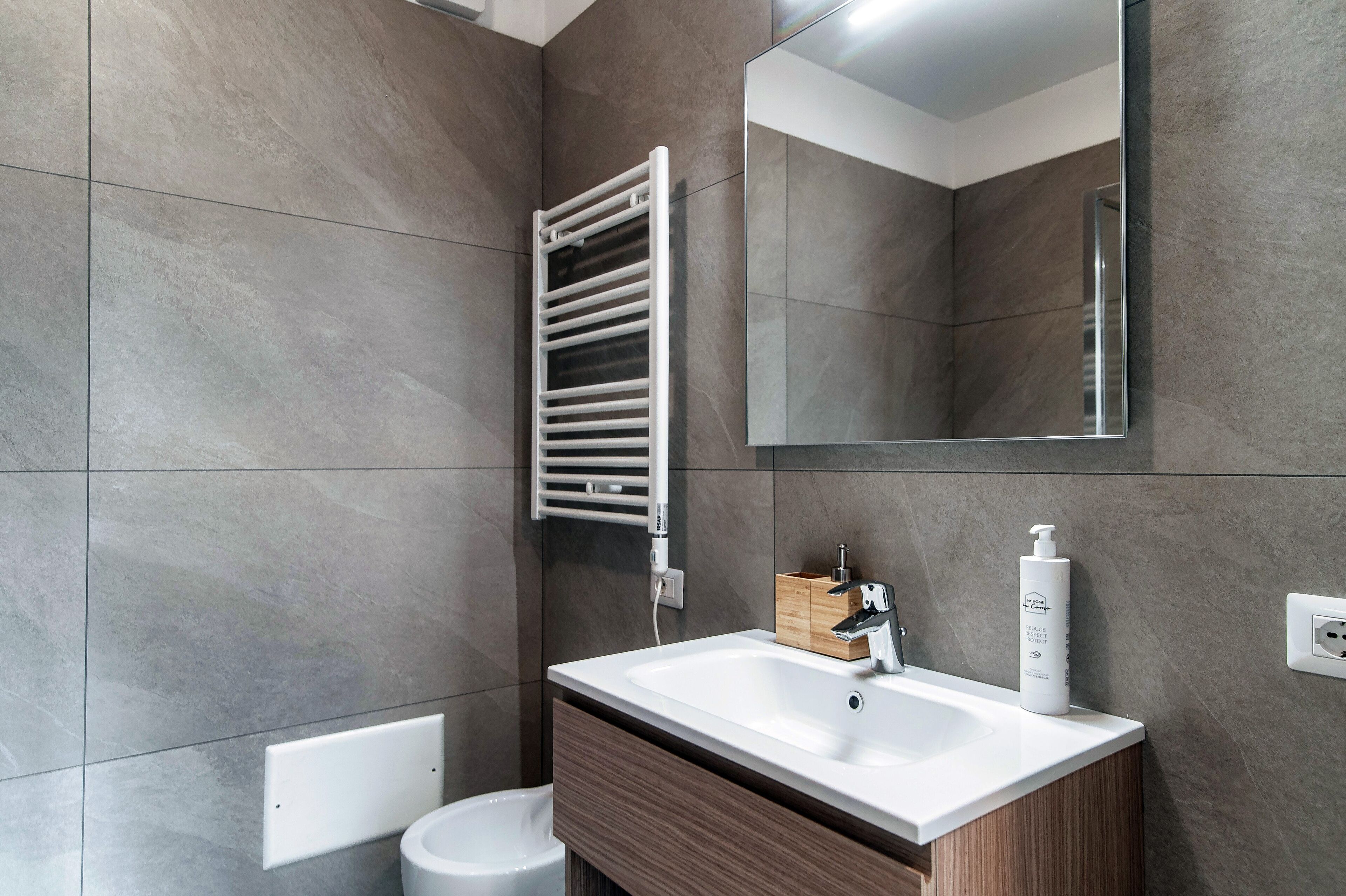 A modern bathroom with a white sink, wooden cabinet, and a towel rack.