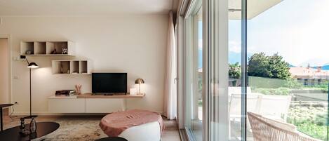 Ein modernes Wohnzimmer mit großem Fenster, einem Flachbildfernseher, einer Couch, einem Couchtisch und einem kleinen Beistelltisch.