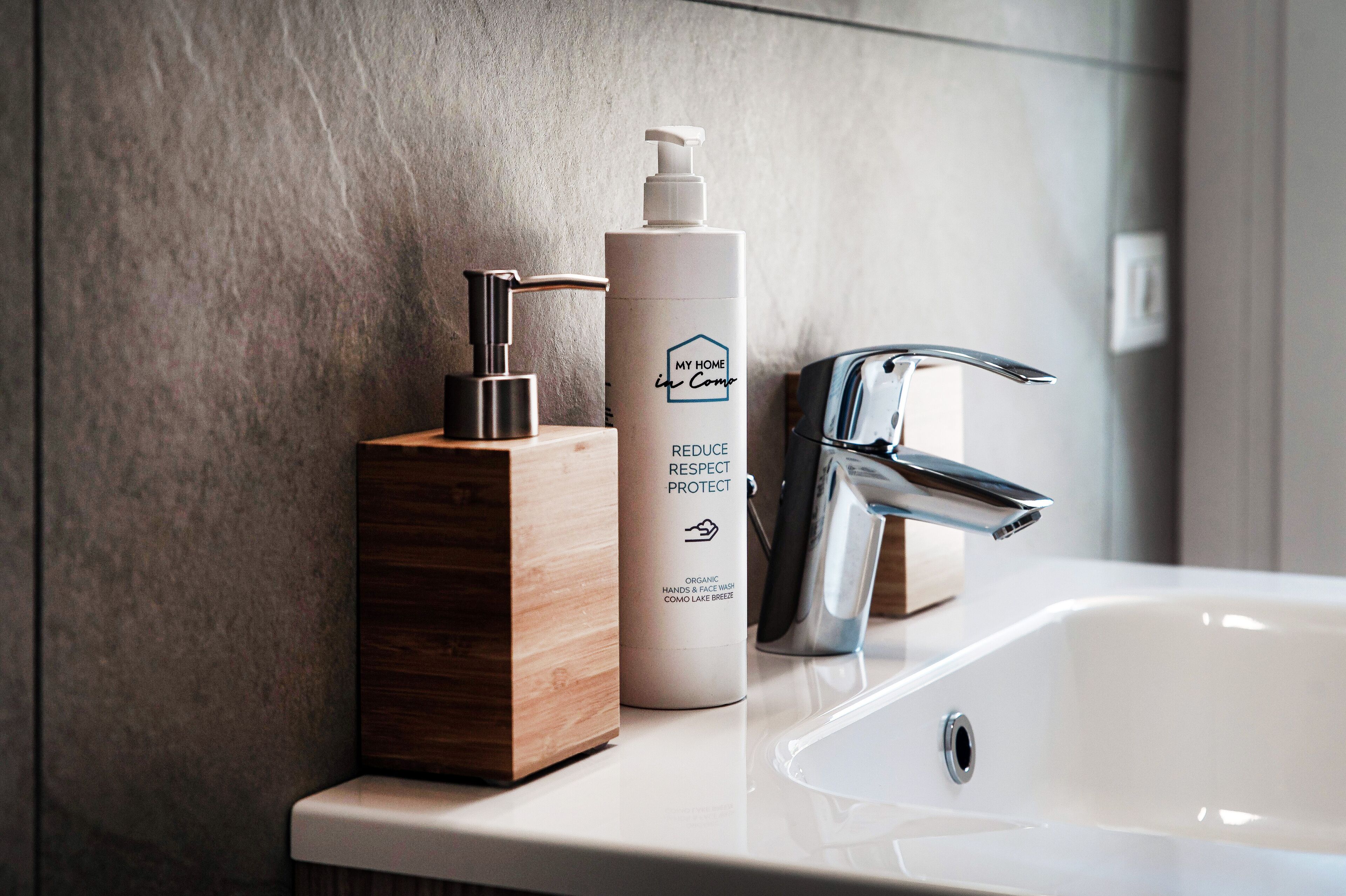A bathroom with a white sink, a wooden soap dispenser, and a bottle of hand soap.