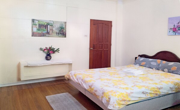 A bedroom with a bed, a wooden door, a small table with a vase of flowers, and a painting on the wall.
