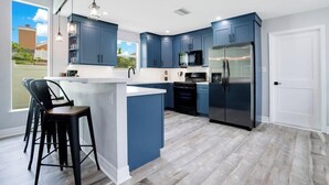 A modern kitchen with blue cabinets, a stainless steel refrigerator, and a bar area with stools. - Spacious 5BR home w/ pool & backyard (Kissimmee)