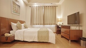 A hotel room with a bed, a desk, a TV, a lamp, and a trash bin. - Enkay Suites - DLF CyberCity (Gurugram)