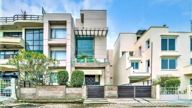 A modern multi-story residential building with a gated entrance, balconies, and a well-maintained garden area. - Enkay Suites - DLF CyberCity (Gurugram)