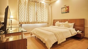 A hotel room with a bed, a desk with a computer, a telephone, and a painting on the wall. - Enkay Suites - DLF CyberCity (Gurugram)