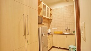 A compact kitchen with wooden cabinets, a stainless steel refrigerator, a microwave, and a sink. - Enkay Suites - DLF CyberCity (Gurugram)