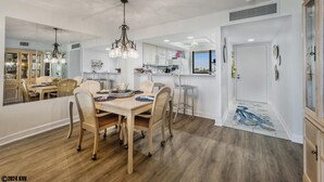 Una cocina moderna con armarios blancos, un comedor con mesa y sillas de madera, y un pasillo con un tapete decorativo.