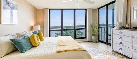 A bedroom with a large bed, a ceiling fan, a view of the outdoors through a sliding glass door, and a dresser with drawers.