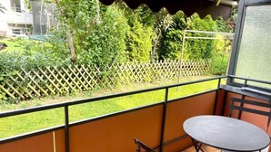 Ein Balkon mit Blick auf einen Garten, ein kleiner Tisch und ein Stuhl.