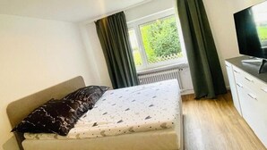 Ein Schlafzimmer mit einem Bett, einem Fernseher, einem Fenster mit Vorhängen und einer Heizung.