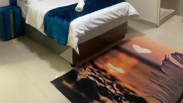 A neatly made bed with white linens and a blue headboard, a blue bedside table, and a painting on the wall. - Sabathlogde VIP  (Cape Town)