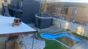 A residential backyard with a swimming pool, a covered patio, and a brick house. - Sabathlogde VIP  (Cape Town)