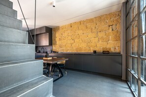 A modern kitchen with a stone wall, grey cabinets, and a dining area with a table and chairs. - Grey House in Zisa by Wonderful Italy (Palermo)