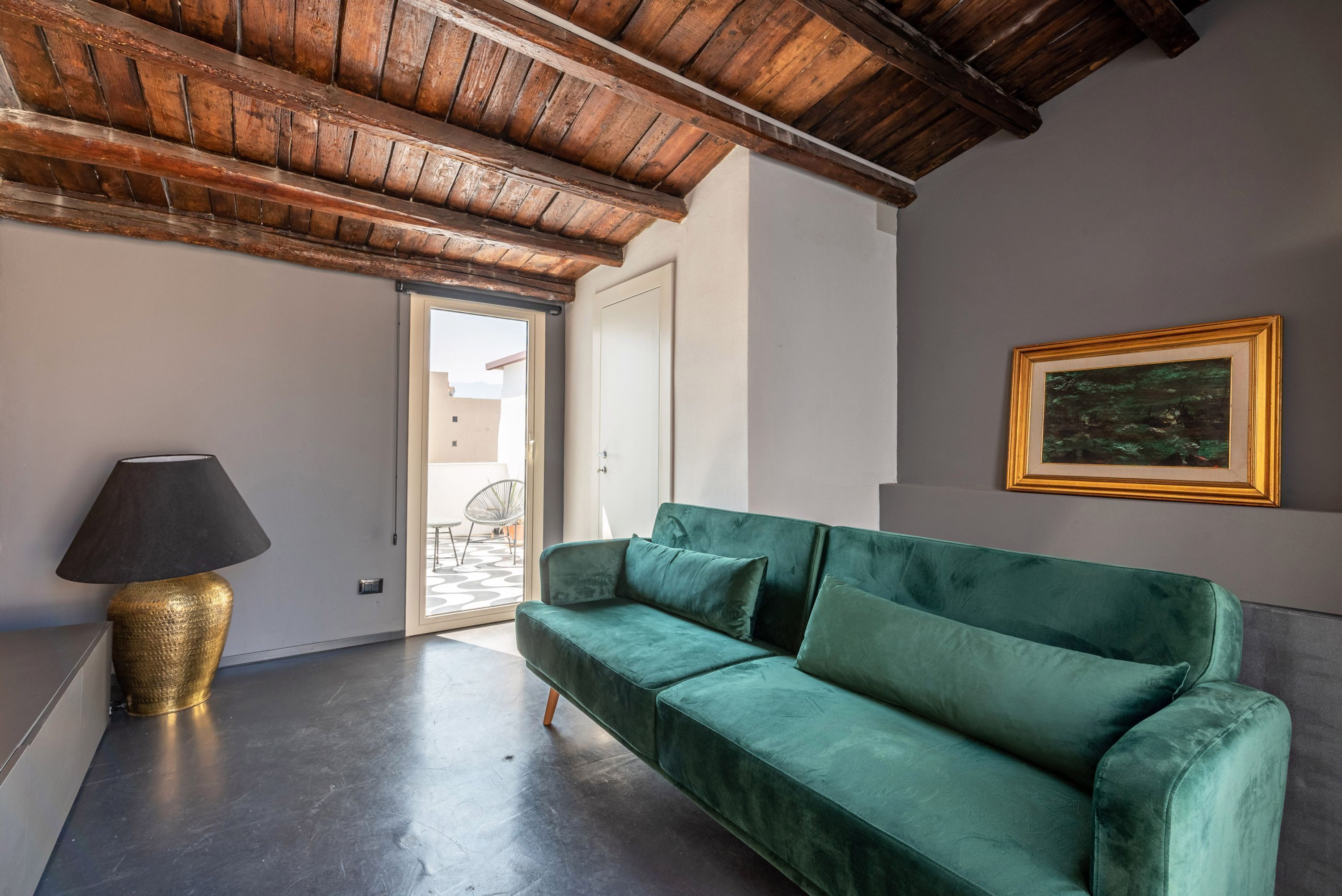 A modern living room with a green sofa, a gold lamp, and a framed painting on the wall.