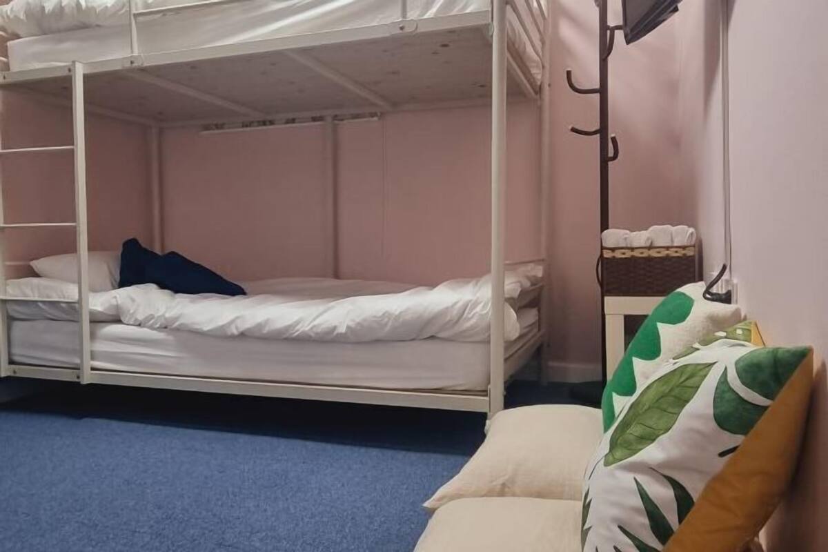 Habitación con literas, alfombra azul, pared blanca y una mesita de noche con una cesta.