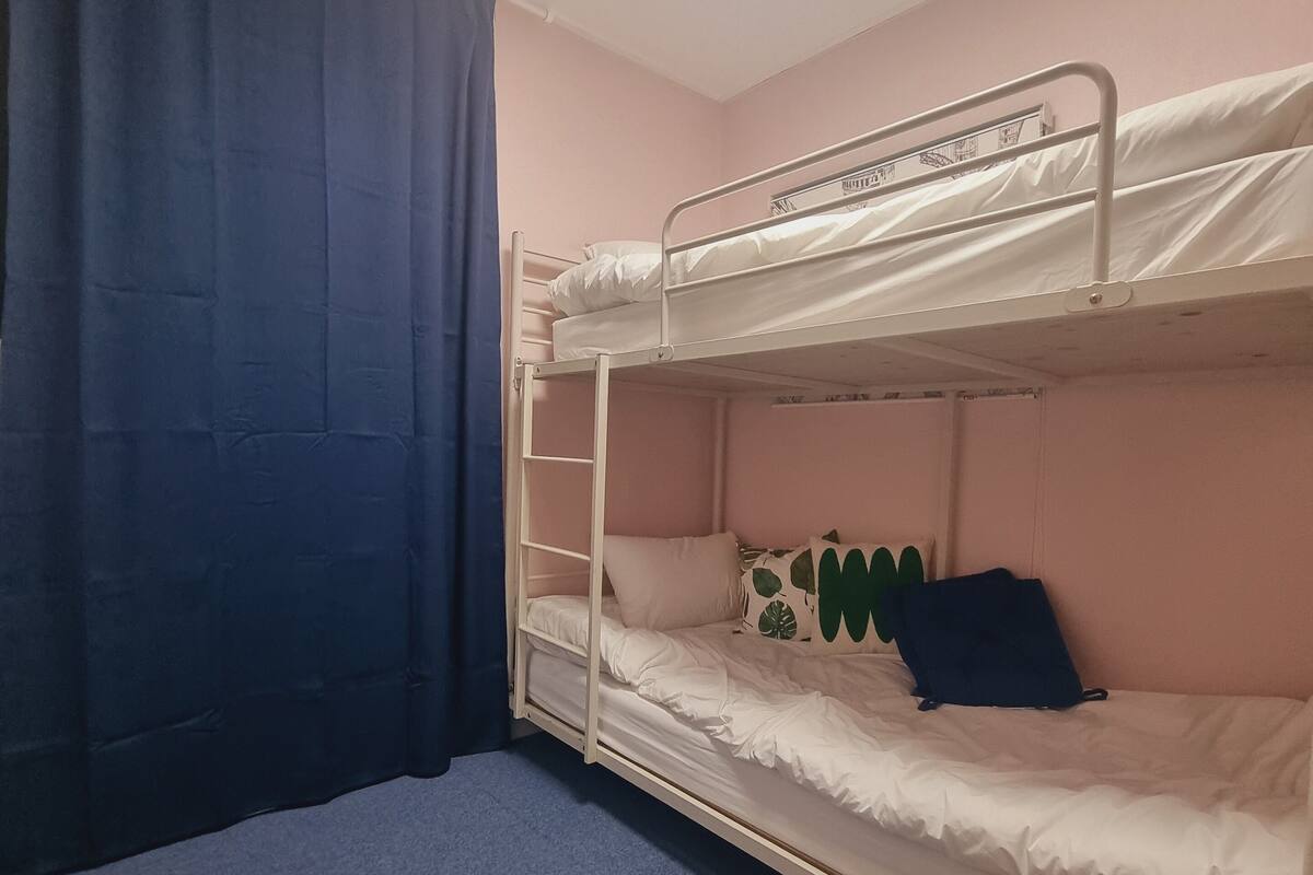 Dormitorio con literas, una cortina azul, una lámpara en el techo y una ventana pequeña.