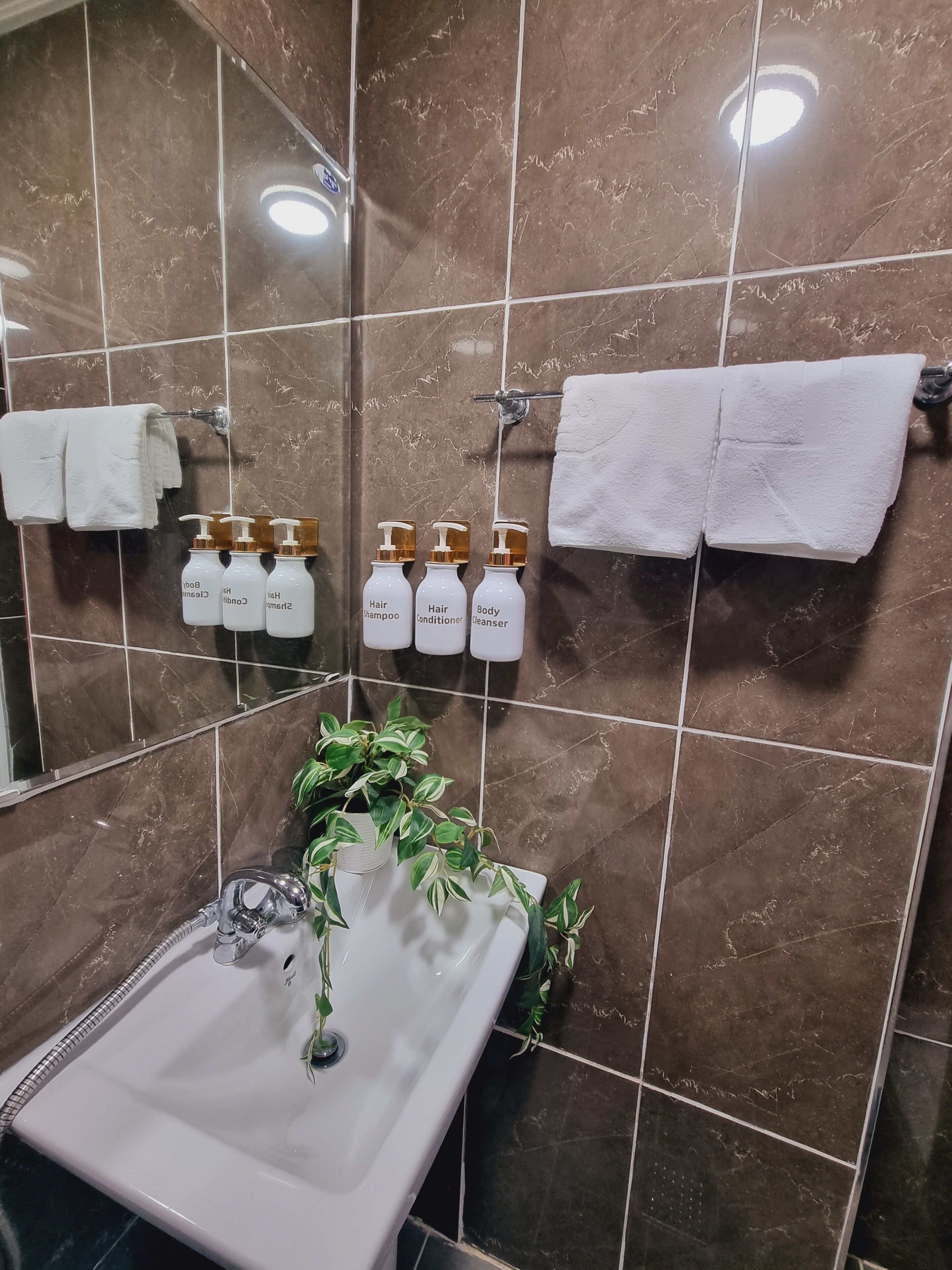 Ein Badezimmer mit einem weißen Waschbecken, braunen Marmorfliesen und weißen Handtüchern an Handtuchhaltern.