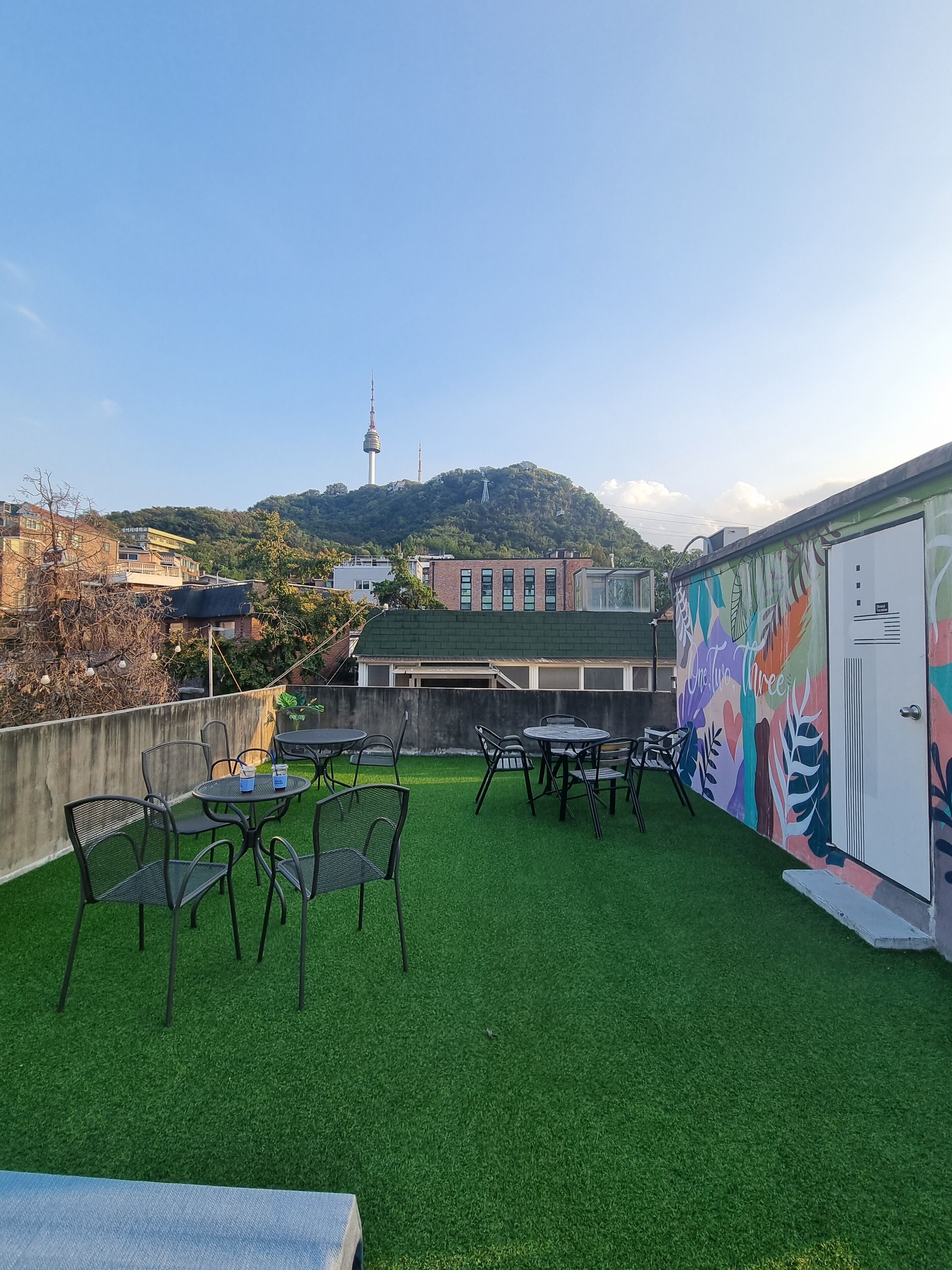 A rooftop terrace with artificial grass, outdoor seating, and a mural.