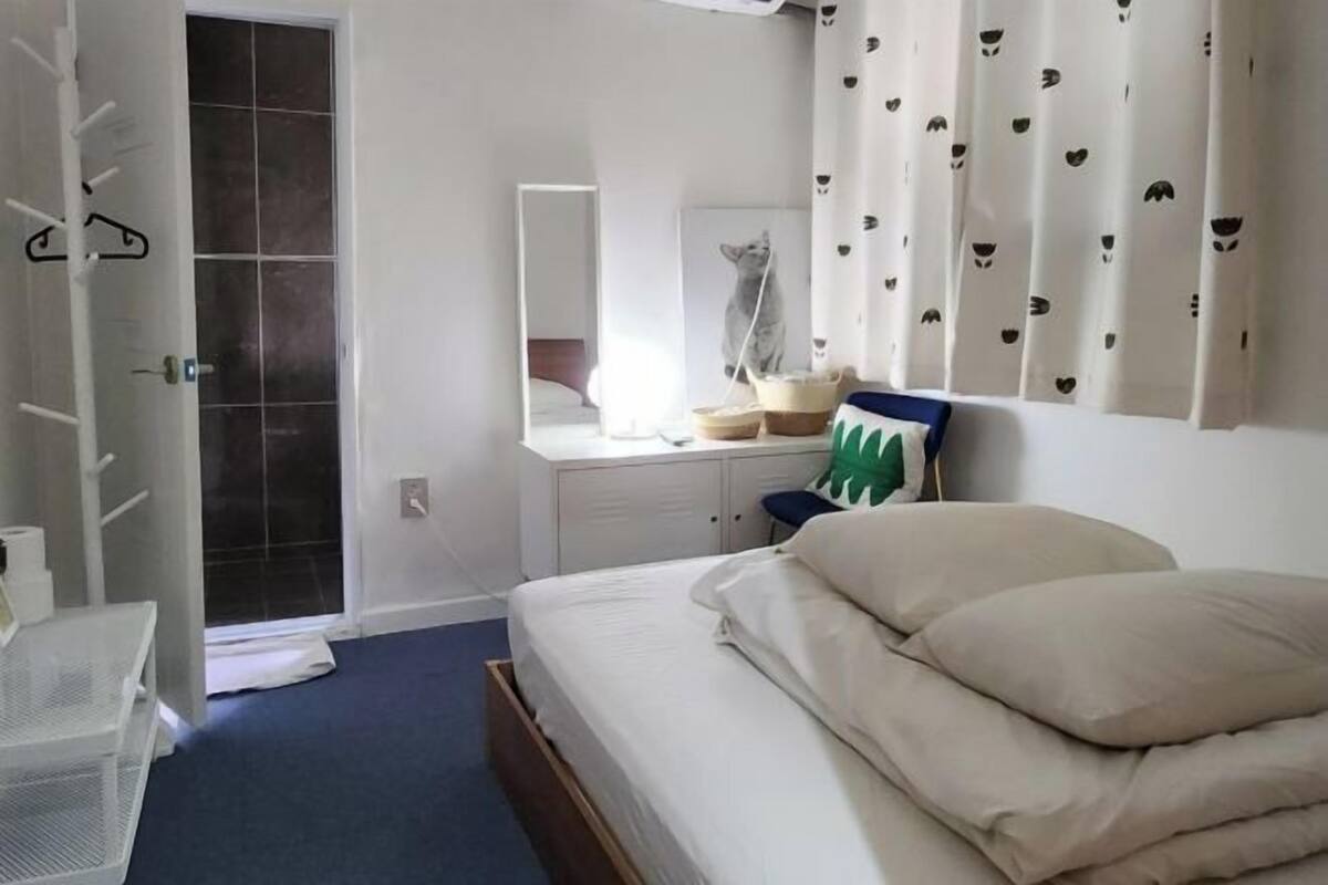 Un dormitorio con cama, cómoda, espejo, ventana con cortinas y puerta.