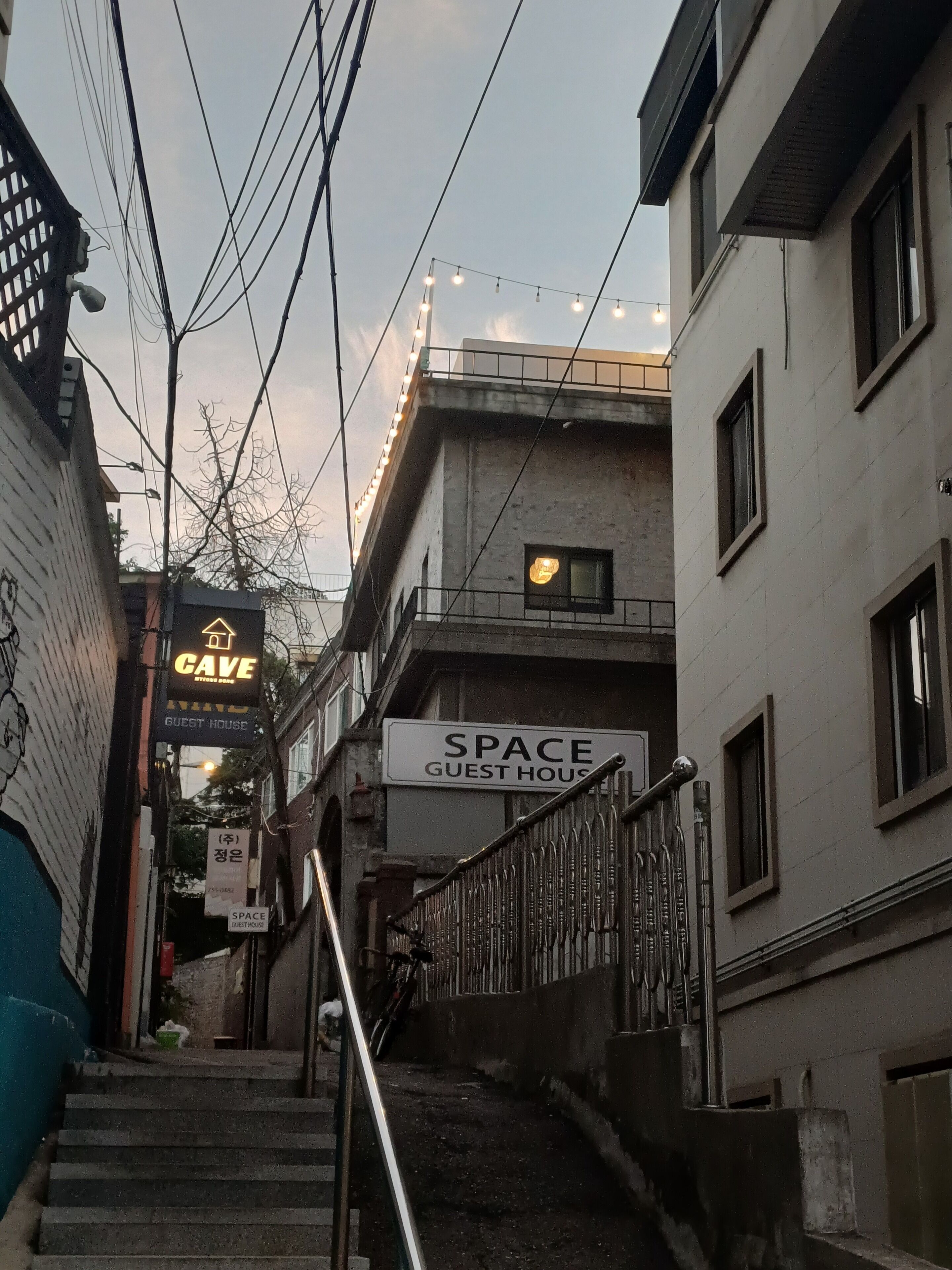 Une ruelle étroite avec un escalier menant à un bâtiment portant l’inscription « SPACE GUEST HOUSE ».