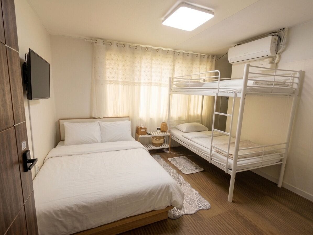 A bedroom with a single bed, a bunk bed, a bedside table, a lamp, and a television.