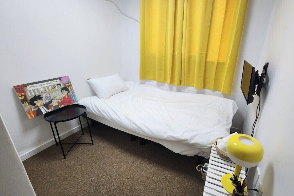 Un dormitorio pequeño y ordenado con una cama individual, una mesita y una silla.
