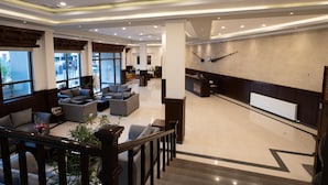 Un vestíbulo amplio con diseño moderno, que incluye una zona de estar con sofás y sillones, un mostrador de recepción y una escalera que conduce a un piso superior.