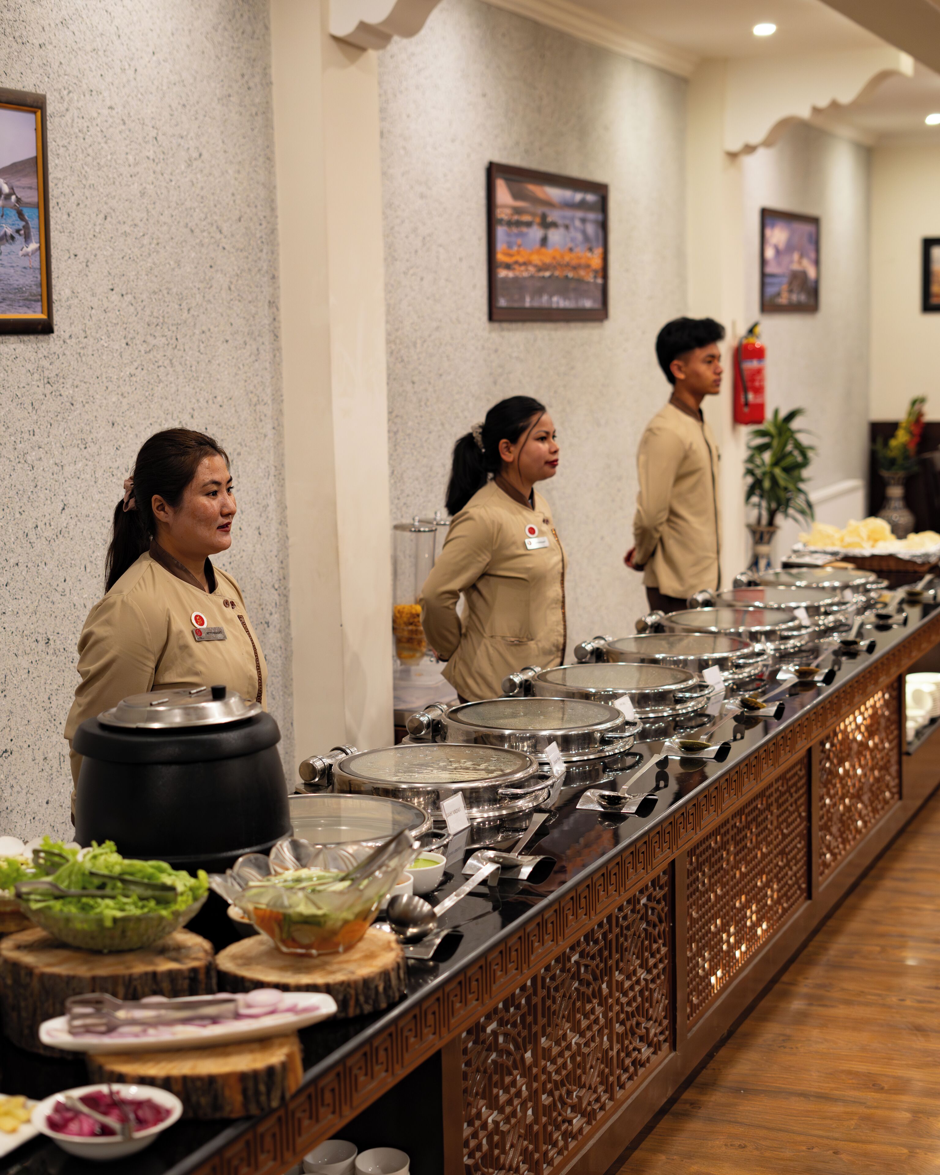A buffet setup with multiple serving stations, a fire extinguisher on the wall, and a decorative plant in the background.