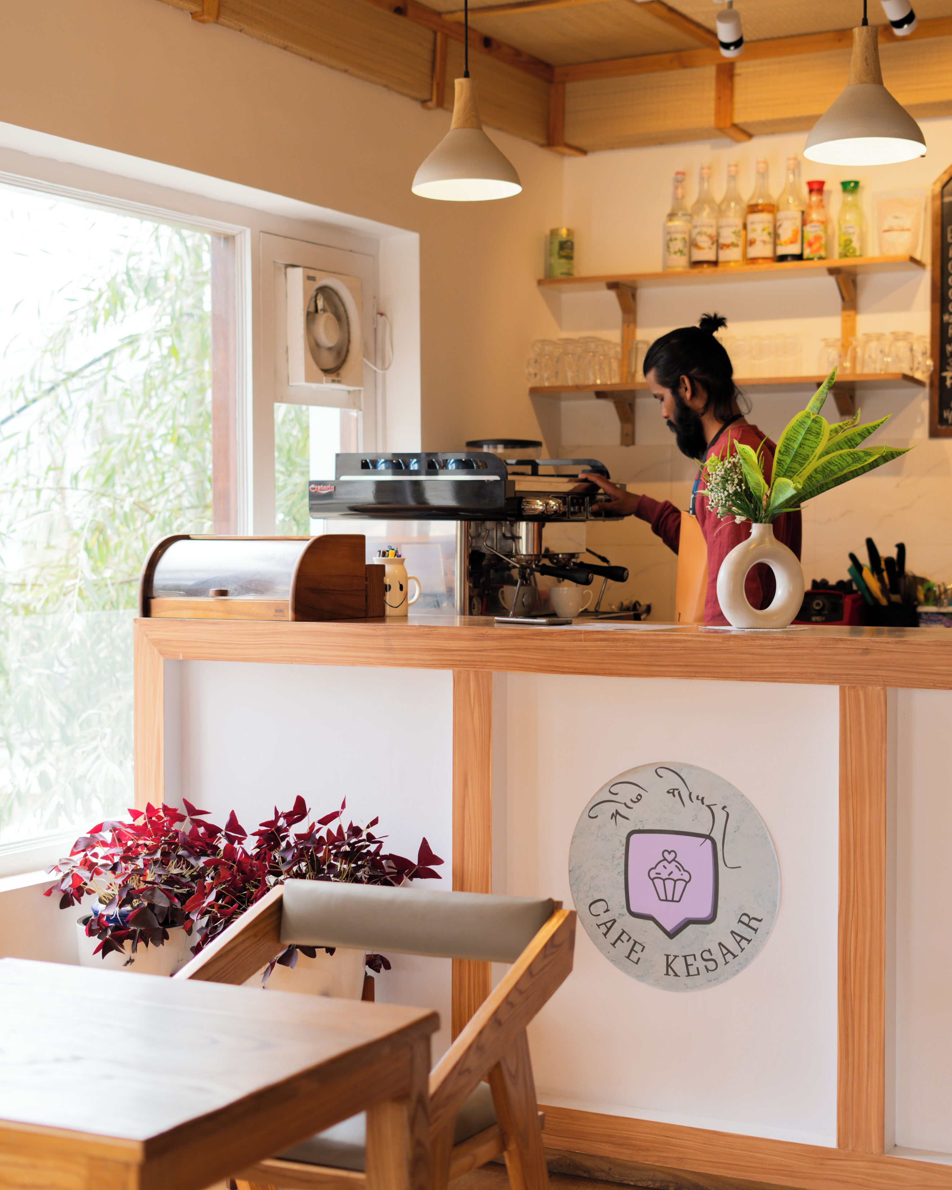 A cafe interior with a coffee machine, a counter, a seating area, and a wall-mounted sign.
