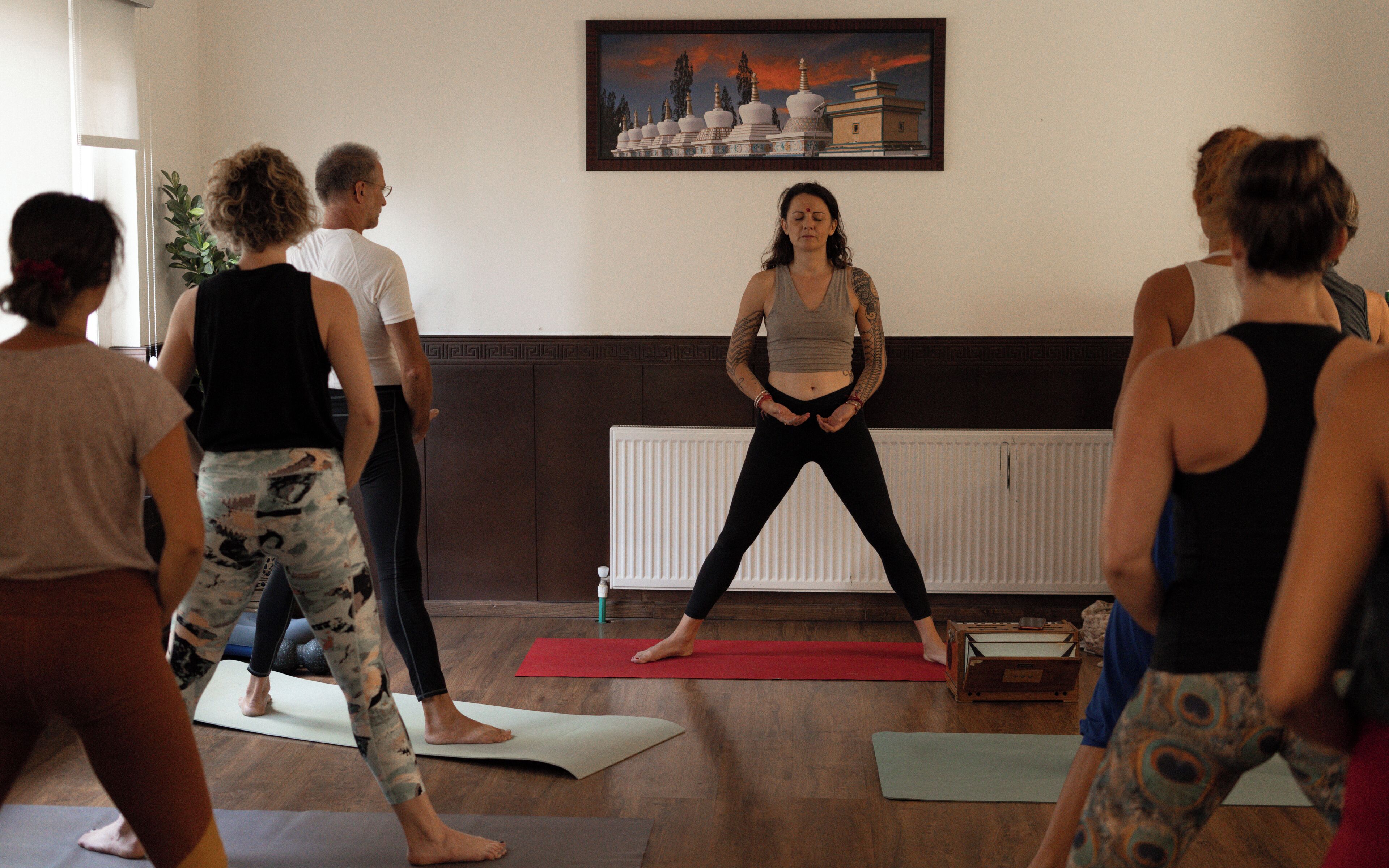 Un grupo de personas practicando yoga en una habitación con pisos de madera y un radiador.