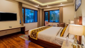Habitación de hotel con una cama grande, un televisor de pantalla plana, un escritorio con lámpara y vistas a un paisaje nevado por las ventanas.