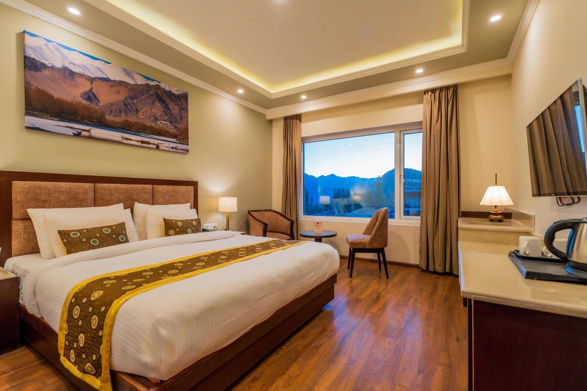 Habitación de hotel con una cama grande, un escritorio, una silla, un ventanal con vista a la montaña y un cuadro en la pared.