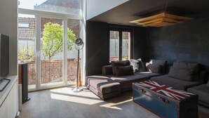 A modern living room with a sofa, a television, and a large window. - Flagey Terrace Design residence (Brussels)