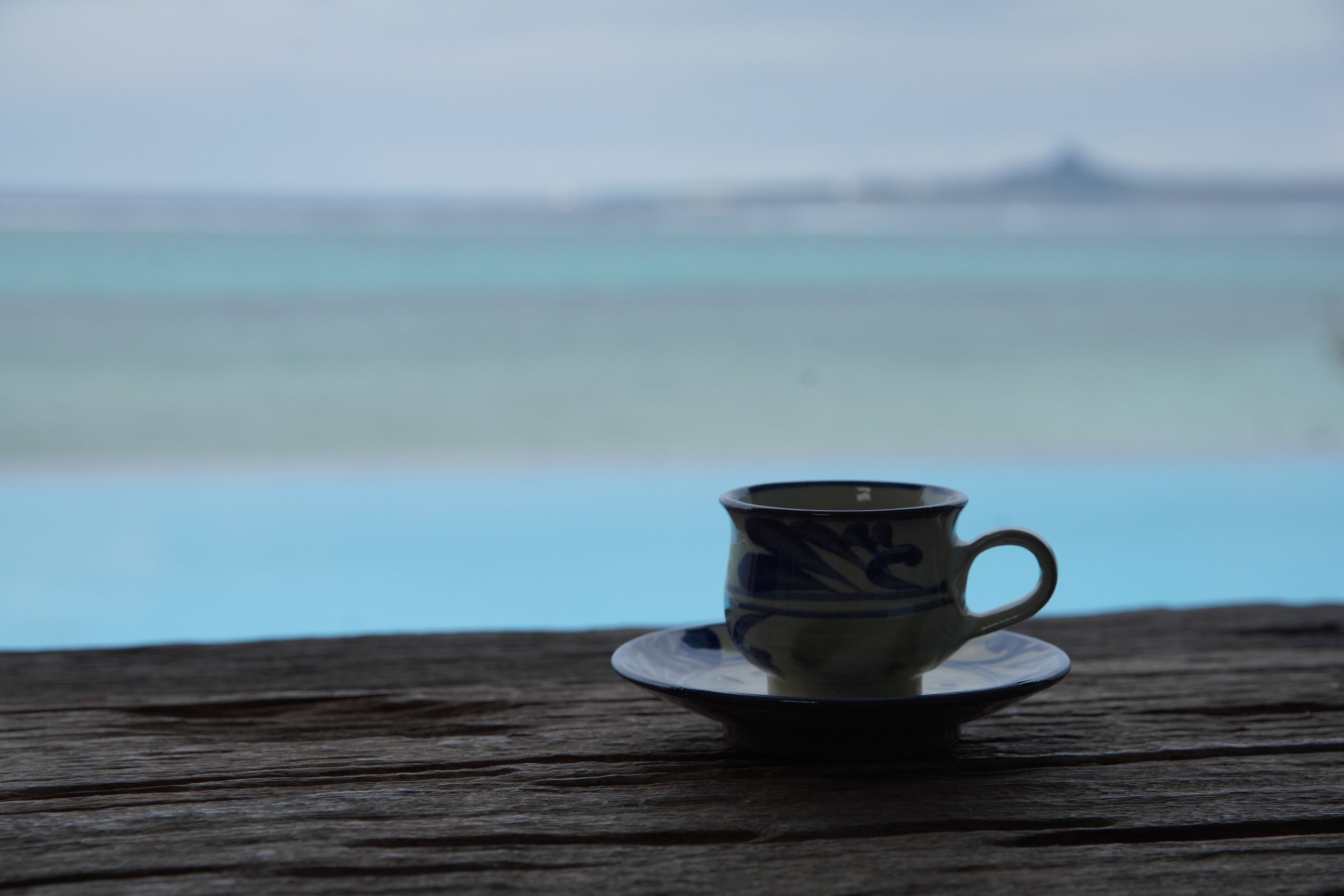 Una taza sobre un platillo en una mesa de madera, con vista al océano.