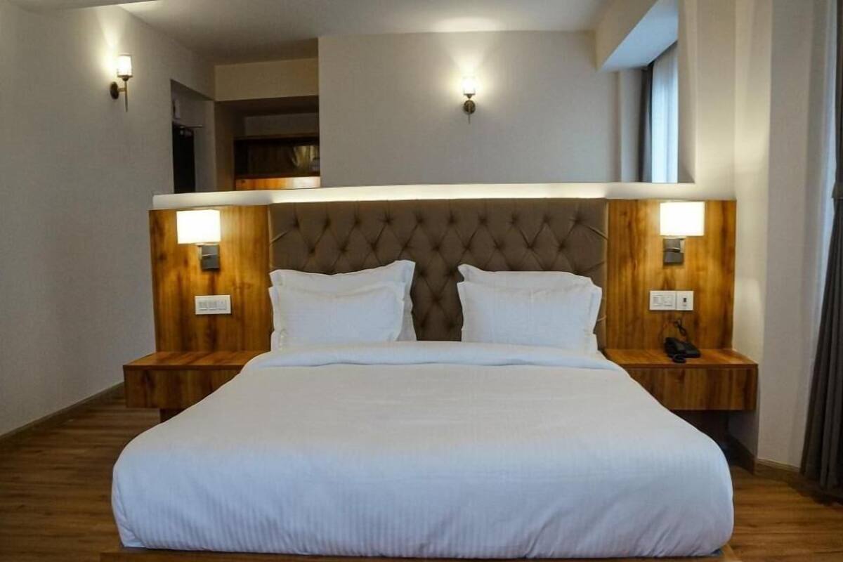 A hotel room with a large bed, wooden headboard, two bedside tables, and wall-mounted lights.