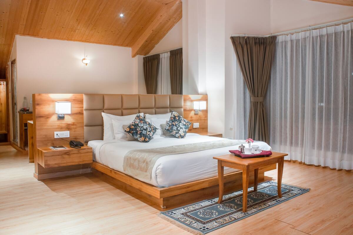 A bedroom with a wooden bed frame, bedside tables, a nightstand, a bedside lamp, a small table with a tray, and a patterned rug.