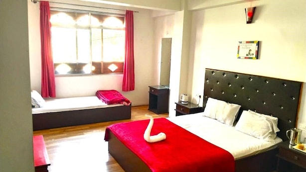 A hotel room with a large bed, a sofa bed, a bedside table with a lamp, and a window with curtains. - BASSU'SHOTEL Silk Route Residency (Gangtok)