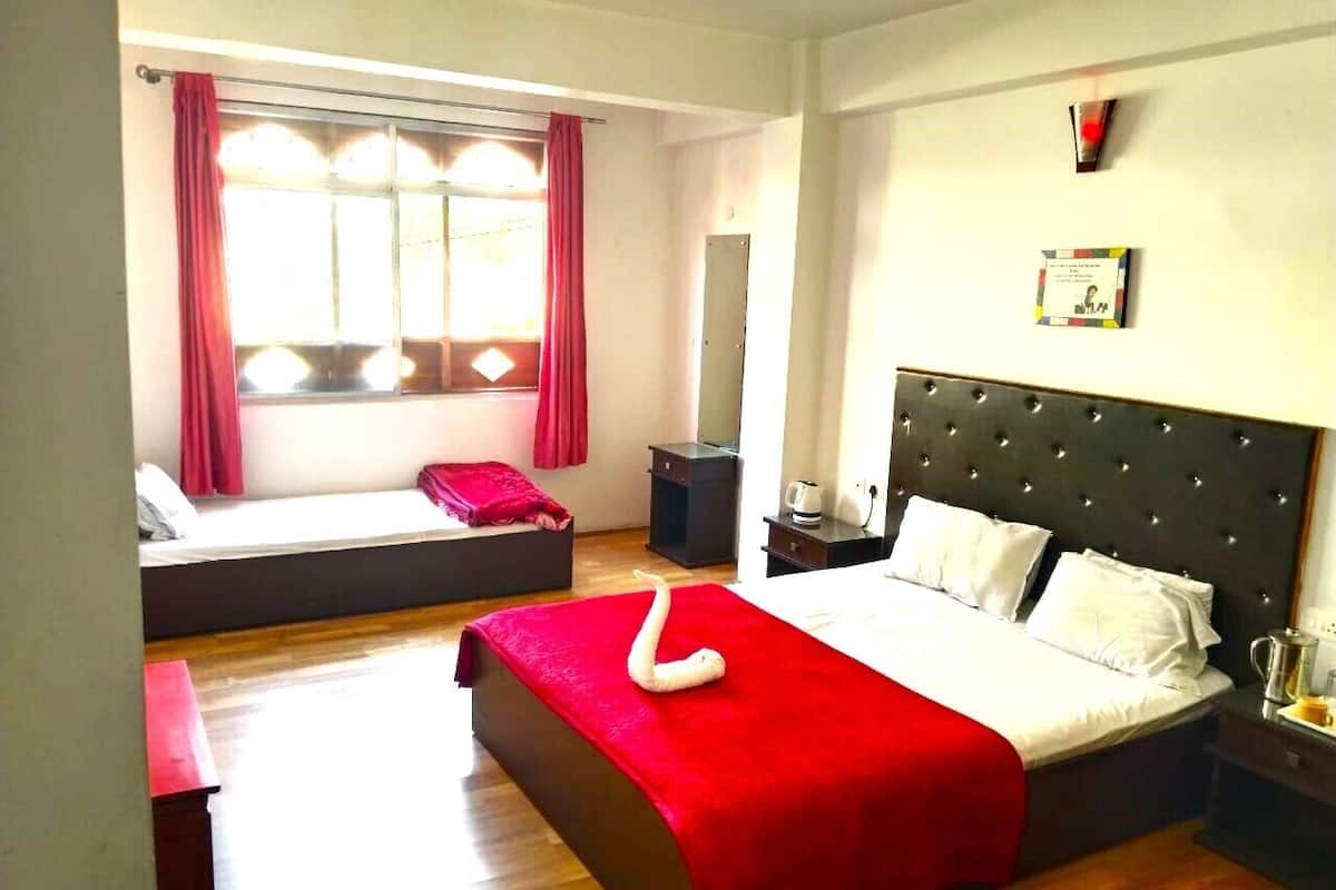 A hotel room with a large bed, a sofa bed, a bedside table with a lamp, and a window with curtains.