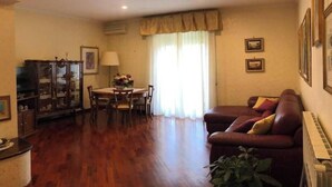 A living room with a wooden floor, a dining table with chairs, a sofa, and a cabinet. - SPACIOUS 90 SQM APARTMENT WITH BALCONIES, PRIVATE PARKING - RAFFAELE DE FERRARI (Roma)