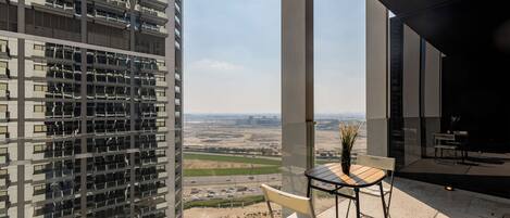Un edificio alto con una terraza que tiene una mesa, sillas, una planta en maceta y vistas del paisaje circundante.