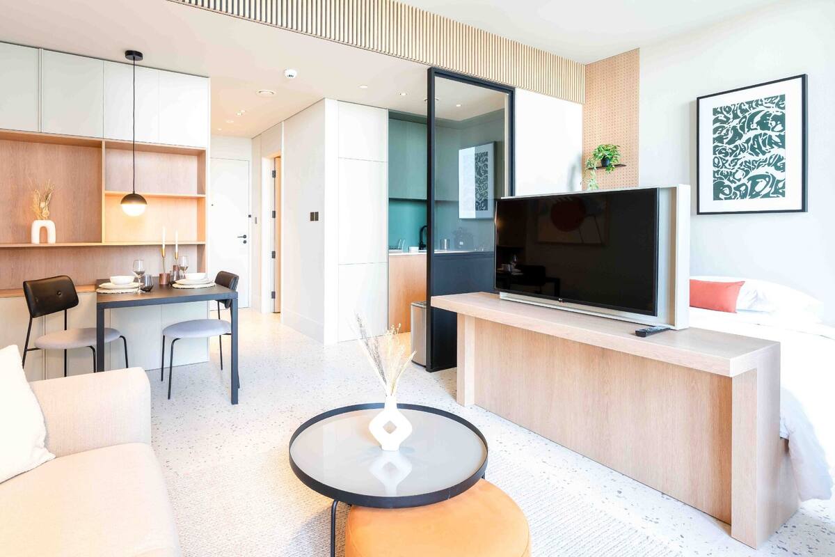 A modern hotel room with a dining area, a TV, and a small round table.